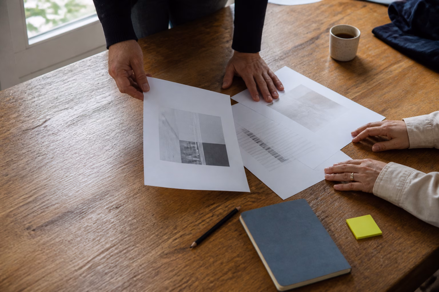 Hands arranging working papers and a notebook on a wooden table